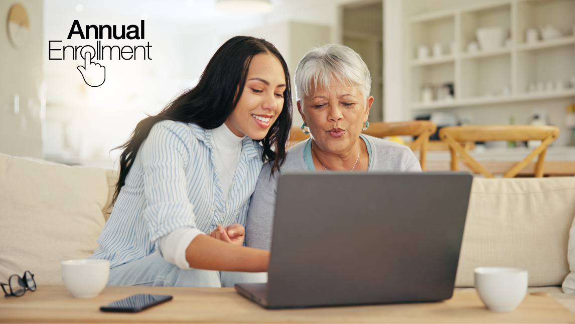 Two women of color sitting on a couch looking together on a laptop. The younger black-haired woman is pointing to the laptop.