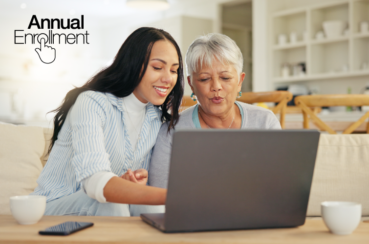 Two women of color sitting on a couch looking together on a laptop. The younger black-haired woman is pointing to the laptop.